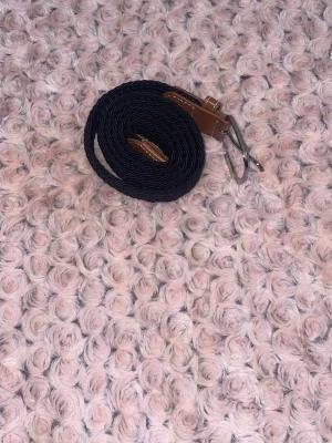 Svart flätat bälte med bruna detaljer - Snyggt svart flätat bälte med bruna skinn-detaljer och silverfärgat spänne. Perfekt för att lyfta vilken outfit som helst och passar till både jeans och byxor. Enkel att justera tack vare det flexibla materialet.