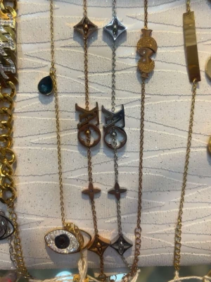 Louis Vuitton halsband i guld och silver - Snygga armband från Louis Vuitton i både guld- och silverfärg. Kedjorna har ikoniska LV-loggor och dekorativa detaljer som stjärnformade hängen och geometriska former. Perfekt accessoar för att lyfta din outfit med en lyxig touch.