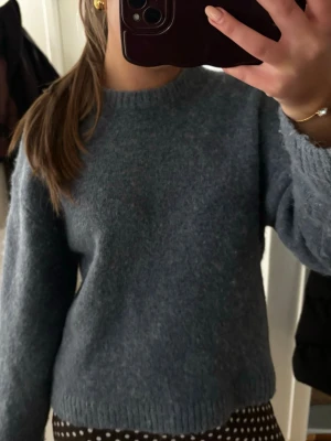 Mörkblå stickad tröja - Mysig mörkblå stickad tröja med rund halsringning och långa ärmar. Tröjan har en enkel, rak passform och ribbstickade muddar vid ärmslut och nederkant. Perfekt för kyliga dagar och lätt att matcha med olika outfits.