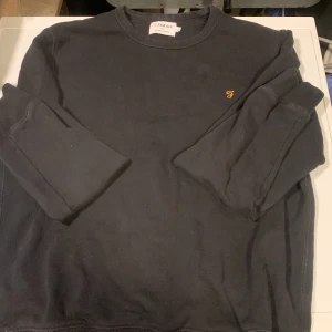 Svart sweatshirt från Farah - Svart sweatshirt från Farah med rund halsringning och liten gul broderad logga på bröstet. Tröjan har ribbade muddar vid ärmslut och nederkant. Perfekt för en avslappnad och stilren look. Satt för tight på mig skulle säga att det är en rätt liten medium