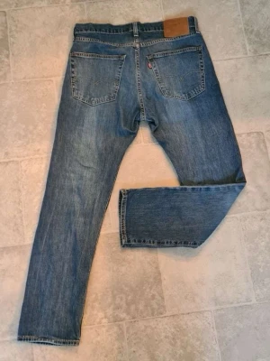 Levi's jeans - Klassiska blå jeans från Levi's med rak passform och fem fickor. Jeansen har en ljus tvätt och tydliga sömmar, samt den ikoniska läderpatchen bak i midjan. Tillverkade i slitstark denim med knappgylf och bälteshällor.