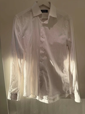 Vit skjorta från Dressmann, storlek S - Klassisk vit skjorta från Dressmann i storlek S. Skjortan har lång ärm, knappar framtill och en stilren krage. Tillverkad i bomull med stretch för extra komfort. Perfekt för dig som vill ha en enkel och clean look.