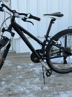Svart Trek mountainbike - Säljer en svart mountainbike från Trek med vita och grå detaljer. Cykeln har dämpad framgaffel, sportig sadel och robust ram. Utrustad med skivbromsar, stänkskärmar och flera växlar. Perfekt för dig som gillar att cykla i olika terränger. 