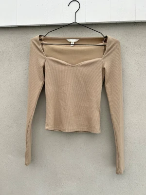 Beige ribbad långärmad topp - Beige tight top med hjärtformad ringning. Endast använd en gång och är som ny. 