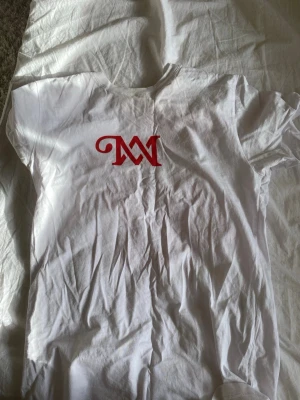 Vit t-shirt We Are Not The Same Tour - Vit t-shirt med rött tryck framtill och stort rött texttryck på ryggen med texten 'We Are Not The Same Tour Part 2'. Klassisk passform och rund hals. Perfekt för dig som gillar statement-plagg och tour-merch.