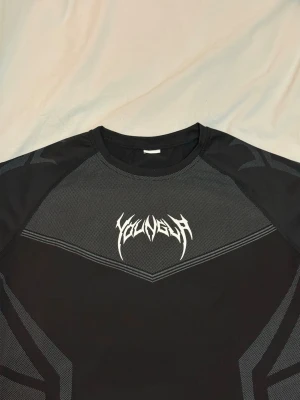 Svart YoungLa t-shirt  - Snygg svart t-shirt i storlek S, från YoungLa med gråa detaljer och ett vitt tryck på bröstet. T-shirten har korta ärmar och sportig design, perfekt för dig som gillar streetwear eller träning. Materialet känns lätt och andas bra.