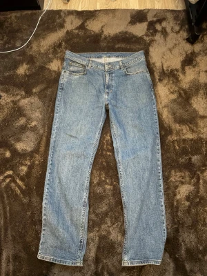 Blå raka jeans från McGordon - Klassiska blå jeans från Levi's med rak passform och fem fickor. Jeansen har en ljus tvätt och tydliga sömmar. Tillverkade i slitstark denim med Levi's ikoniska läderpatch bak i midjan. Perfekta för en avslappnad och tidlös look.