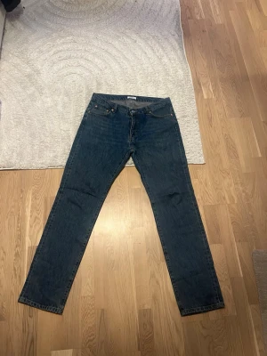 Mörkblå raka jeans - Säljer ett par klassiska mörkblå jeans med rak passform och fem fickor. Jeansen har en enkel design utan slitningar och är perfekta för en clean och tidlös look. Passar dig som gillar basic och stilrent.