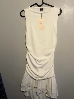 Vit volangklänning från Shein - Snygg vit klänning från Shein med volangdetaljer nedtill och ärmlös design. Klänningen har en draperad passform och är tillverkad i ett mjukt, stretchigt material som ger en bekväm känsla. Passande inför studenten.