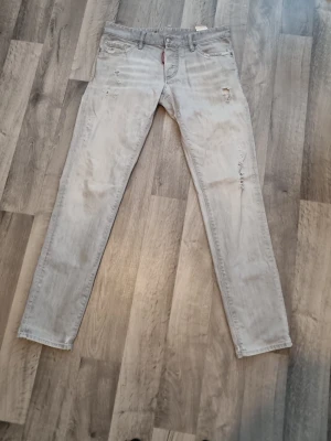 Ljusgrå skinny jeans från Dsquared2 - Säljer ett par ljusgrå skinny jeans från Dsquared2 med slitningar och distressed detaljer på benen. Klassisk femficksmodell med knappgylf och cool tvätt. Perfekta för dig som gillar streetwear och vill ha en trendig look.