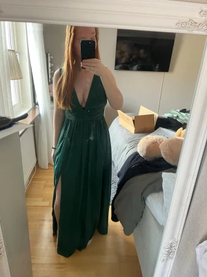 Mörkgrön plisserad balklänning med slits - Säljer min superfina balklänning med djup v-ringning fram och bak, och slits på sidan som gör den väldigt enkel att gå i. Klänningen har breda axelband och markerad midja som ger en smickrande siluett. Perfekt för till exempel bal! Hittar ingen storlekslapp men skulle säga att det är 36/38. 