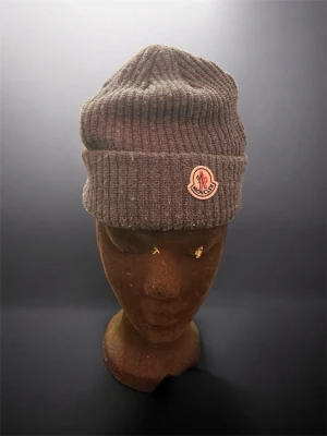 Mörkgrå ribbstickad mössa - Säljer en mörkgrå ribbstickad mössa  med uppvikt kant och det klassiska emblemet framtill. Mössan är i mjukt material och har en tidlös, enkel design som passar perfekt till kalla dagar.