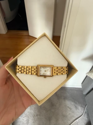 Guldfärgad klocka från Mockberg - Stilren guldfärgad klocka från Mockberg med rektangulär urtavla och länkarmband i metall. Urtavlan är vit med guldiga detaljer och romerska siffror. Extra länkar medföljer så du kan justera storleken. Perfekt accessoar för en elegant look. Lite defekter på färgen som man kan se på de två sista bilderna men inget som märks av!