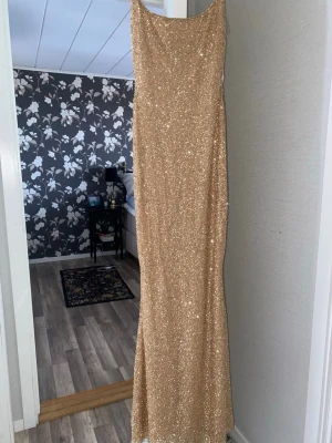 Glittrig långklänning med smala band - Snygg långklänning i guld med smala axelband och glittriga paljetter över hela klänningen. Klänningen har en figurnära passform och är perfekt för speciella tillfällen. Materialet känns mjukt och följsamt. Tyvärr var klänningen för lång för mig:(lapp kvar