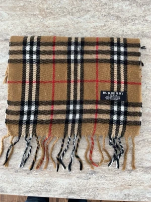 🤎 Burberry halsduk – Beige – Klassisk & tidlös lyx 🤎 - Säljer en elegant Burberry halsduk i klassisk beige färg – ett riktigt statement-plagg som aldrig går ur stil. Den neutrala tonen gör den enkel att matcha med allt från svart kappa till ljusare höstlooks.  Den ikoniska designen ger en exklusiv och sofistikerad känsla. Perfekt för dig som gillar clean, old money / minimalistisk stil.  ✔️ Beige – lätt att matcha ✔️ Tidlös & lyxig design ✔️ Passar både dam & herr ✔️ Perfekt till höst & vinter ✔️ Höjer vilken outfit som helst 
