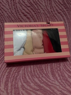 Flerpack trosor Victoria's Secret - Säljer ett flerpack trosor från Victoria's Secret i olika färger: vitt, beige, ljusrosa, rött och svart. Trosorna är ribbade med spetsdetaljer och har logotypen tryckt i midjeresåren. Perfekta för dig som vill ha både stil och komfort.