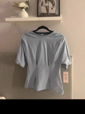 Ljusblå topp med kort ärm från nelly - Snygg ljusblå topp från nelly med korta ärmar och rund halsringning. Toppen har en lätt figursydd passform och är gjord i mjuk bomull, perfekt för en chill och stilren look.