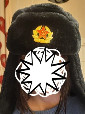 Svart ushanka med sovjetmärke - Klassisk svart ushanka med öronlappar och ett broderat sovjetiskt emblem framtill som smidigt går att ta bort. Hatten är gjord i mjuk, pälsliknande syntetmaterial och har en tydlig röd stjärna med hammare och skära på framsidan. Inköpt 2024 från *Röda stjärnan * använd 1gång. Pris kan diskuteras. Inköpt för 600,går på 350 på deras hemsida för tillfället. 