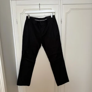 Svarta kostymbyxor från Bläck,  - Snygga svarta kostymbyxor från Bläck i storlek M. Klassisk rak passform med diskreta fickor och bälteshällor. Tillverkade i en mjuk bomullsblandning som känns skön mot huden. Perfekta för en clean och stilren look.