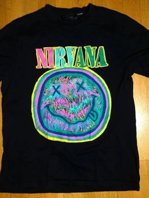Nirvana T-Shirt | M / Medium - T-Shirt med Nirvana på framsidan.  Nirvana X HM (2023). Medium (Mått finns på bilderna!) 100% bomull.  Se bilder.
