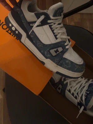 Louis Vuitton blåvita sneakers - Säljer ett par Louis Vuitton sneakers i blått och vitt med klassiskt monogrammönster. Skorna har vita snören, detaljer i mörkblått och vitt samt LV-logga på sidan och hälen. Tillverkade i en mix av läder och textil för en exklusiv känsla. Lite smutsiga  under annars bra 