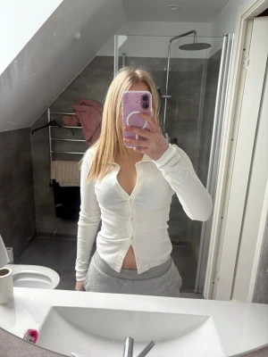 Vit ribbad topp med knappar från Nelly - Snygg vit ribbad topp från Nelly med lång ärm och v-ringning. Toppen har knappar framtill och är croppad vilket ger en trendig look. Perfekt att styla med jeans eller kjol för en fräsch outfit.