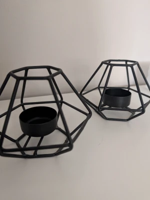 Svarta geometriska ljushållare - Två svarta ljushållare i metall med modern, geometrisk design. Perfekta för värmeljus och ger en stilren känsla till rummet. Passar snyggt på hylla, bord eller fönsterbräda. Säljes som par.