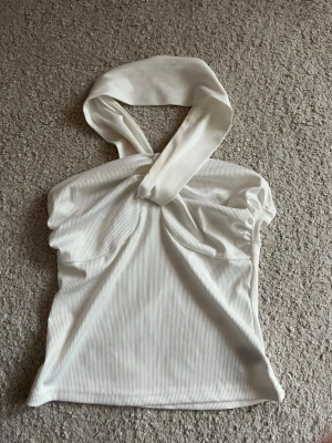Vit ribbad halterneck topp - Trendig vit ribbad halterneck topp med twistad detalj framtill. Toppen är ärmlös och har en snygg omlottkänsla vid halsen. Perfekt för dig som gillar stilrena och moderna plagg. Materialet känns mjukt och stretchigt.