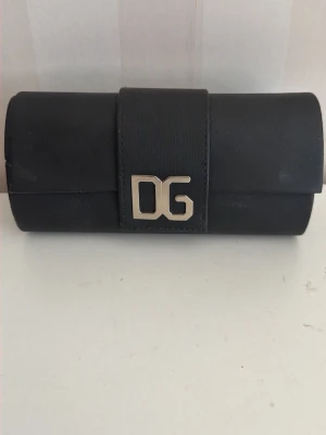 Turkosa solglasögon från Dolce & Gabbana - Snygga solglasögon från Dolce & Gabbana med turkosa bågar och mörka glas. Kommer i ett svart fodral med DG-logga i silver. Perfekt accessoar för att lyfta din stil med en färgklick och exklusiv känsla.