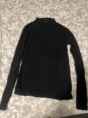 Svart polotopp från Gina Tricot - En svart långärmad polotopp från Gina Tricot i mjukt och stretchigt material. Perfekt att styla med jeans eller kjol för en clean och enkel look. Polokrage och figurnära passform ger en snygg siluett.