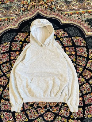 Ljusgrå hoodie med magficka - Säljer en stilren ljusgrå hoodie i mjuk bomullsblandning. Hoodien har en stor huva, ribbade muddar och en klassisk magficka framtill. Perfekt för en avslappnad och trendig look.