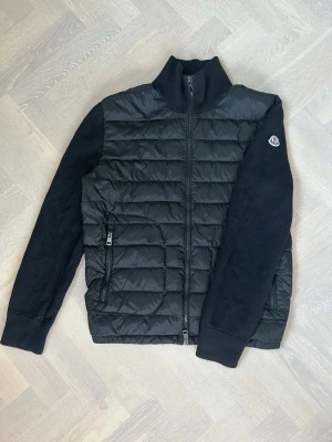 100% äkta Moncler Cardigan - Svart Moncler Tricot Down Cardigan | Nypris: 10 000kr | Size: L | Skick: 8/10 | Aktenhetsbevis från GarmsMarket (se bild) | Hör av dig vid minsta fråga eller fundering// Den är tvättad hårt, observera att den är liten i storleken!
