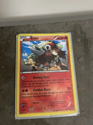 Pokémonkort Entei holografisk - Säljer ett Pokémonkort med Entei, holografisk version. Kortet har röd och gul ram, med Entei illustrerad i mitten och text på engelska. Kortet är inplastat och har attacker som Burning Roar och Combat Blaze.