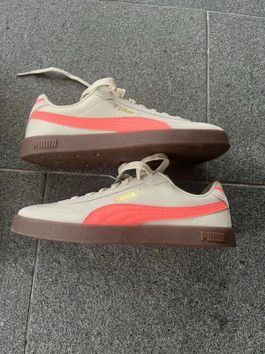 Puma sneakers beige och korall - Snygga sneakers från Puma i beige med korallrosa sidodetalj och bruna sulor. Klassisk låg modell med snörning och guldfärgad Puma-logga på sidan. Helt oanvänd och köpta för 700