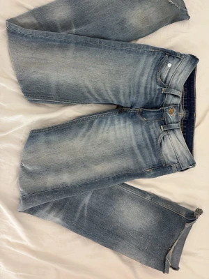 Ljusblå jeans från Cheap Monday - Säljer ett par ljusblå jeans från Cheap Monday med snyggt slitna detaljer och klassisk femficksmodell. Jeansen har en vit patch med Cheap Monday-loggan bak på linningen och är tillverkade i bomull. Perfekta för en avslappnad streetstil.