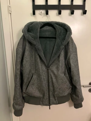 Grå teddyjacka från Zara dubbel sidig - Mysig grå teddyjacka med stor huva och dragkedja framtill. Jackan har fyra snedställda fickor och ribbade muddar vid ärmslut och midja. Insidan är fodrad med mjuk teddy, perfekt för kyliga dagar. Snygg och avslappnad passform. Jackan går att vända ut och in 