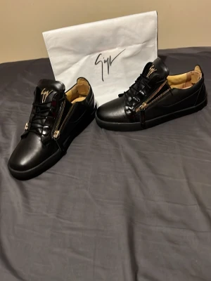 Svarta sneakers från Giuseppe Zanotti - Svarta sneakers i läder från Giuseppe Zanotti med guldfärgade dragkedjor på sidorna skorna är i bra skick 8/10 hör av dig för mer bilder dustbag tillkommer riktigt feta skor!!! Serienummer stämpel och så vidare finns ine i skorna 