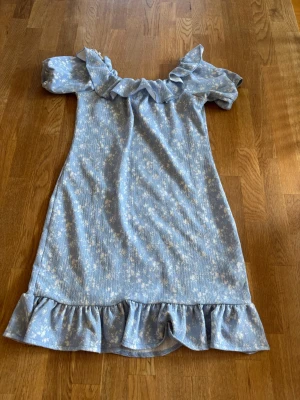 Blå blommig volangklänning Gina Tricot - Supersöt blå kortklänning från Gina Tricot med vita blommor, volang vid axlar och nederkant. Offshoulder-modell i mjukt, ribbat material som känns lätt och somrigt. Perfekt för dig som gillar romantiska detaljer och en avslappnad stil.