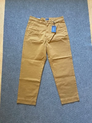 Helt ny GANT chinos herr W31 brun bomull - Bruna chinos från GANT i bomull, herrmodell i stl 48/W31. Knapp och gylf fram, snedställda fickor fram och bakficka med knapp.  Storlek:31 Mått: Midja 40cm Innerben 68cm Fotvidd 20cm  Nypris 1300kr