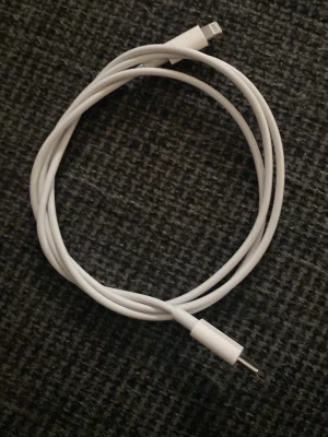 Vit Lightning till USB-C kabel - Säljer en vit laddningskabel med Lightning-kontakt i ena änden och USB-C i andra. Perfekt för att ladda och synka din iPhone eller iPad. Kabeln är flexibel och har en slät plastyta som gör den enkel att använda till vardags.