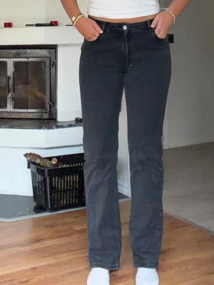 Svarta raka jeans med mellan hög midja  - Snygga svarta jeans med rak passform och hög midja. Jeansen har klassisk femficksdesign och stängs med knapp och dragkedja. Perfekta för en stilren och avslappnad look.
