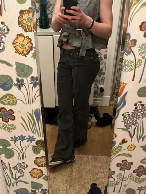 Svarta bootcut jeans med låg midja - Säljer ett par svarta bootcut jeans med låg midja och klassiska fem fickor. Jeansen har en snygg utsvängd passform och stängs med knapp och dragkedja. Perfekta för en trendig och avslappnad look.