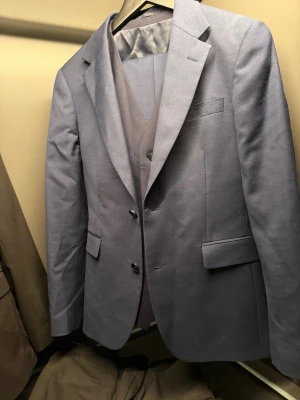 Blå kostym med väst - Snygg blå kostym med matchande byxor från dressman. Klassisk kavaj med två knappar, ficklock och smal krage. Perfekt för dig som vill ha en stilren och modern look. Kostymen har en elegant passform och är lätt att matcha med skjorta och slips. Köpt ny för 2000kr använd ett enstaka gånger 