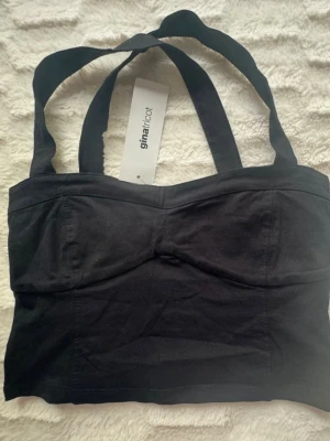 Ny.Svart croppad linnetopp Gina Tricot - Snygg svart croppad linnetopp från Gina Tricot med breda axelband och markerad byst. Toppen är enkel och stilren, perfekt att matcha med jeans eller kjol. Tillverkad i mjuk bomull för en bekväm känsla.