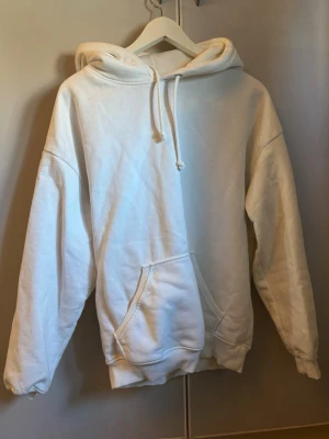 Vit oversized hoodie med ficka - En stilren vit hoodie med huva och dragsnören. Hoodien har en stor magficka och ribbade muddar vid ärmslut och nederkant. Perfekt för en avslappnad och trendig look. Materialet känns mjukt och bekvämt, passar perfekt till jeans eller mjukisbyxor.