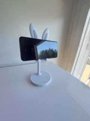 Kanin Mobilhållare - Denna mobilhållare är utformad som en kanin och är perfekt för att hålla din telefon. Den är enkel att montera och demontera, vilket gör den praktisk att ta med sig. Hållaren är stabil och kan användas för att titta på videor, ringa videosamtal eller bara förvara din telefon på ett organiserat sätt.