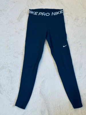 Svarta Nike Pro leggings - Snygga svarta Nike Pro leggings med Nike-logga. Tight passform och stretchigt material som passar perfekt till träning eller chill. Liten vit Nike Swoosh på benet ger en sportig look.