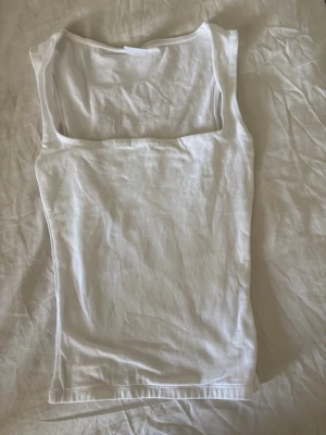 Vit linnetopp från Gina Tricot - Säljer en vit, enkel och stilren linnetopp från Gina Tricot. Toppen har en rak, något tight passform och är ärmlös med breda axelband. Perfekt att matcha med jeans eller kjol för en clean look.