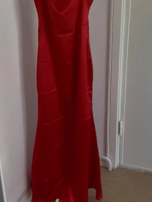 Långklänning i satin - Säljer en elegant röd långklänning i glansigt satinmaterial. Klänningen har en enkel, figurnära siluett och är ärmlös med smala axelband. Perfekt för bal eller festliga tillfällen. Skriv vid frågor 
