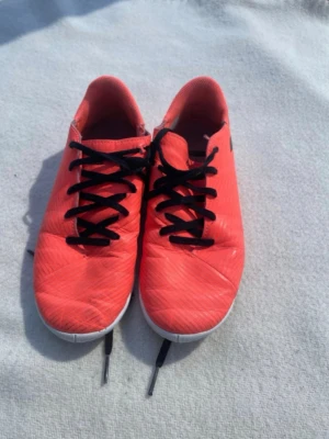 Adidas Nemesis fotbollsskor orange - Säljer ett par Adidas Nemesis fotbollsskor i en snygg orange färg med svarta snören och grå sula. Skorna har en låg profil och är designade för inomhusspel. Materialet är syntetiskt och sulan har bra grepp för snabba vändningar på planen.
